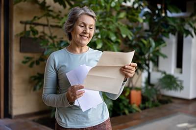 older woman standing outside at home reading a letter